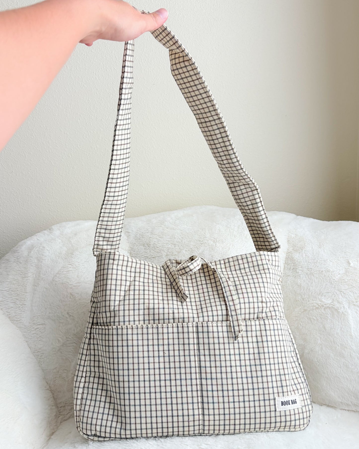 Plaid patterned handbag with a checkered strap held by a person on a white surface.