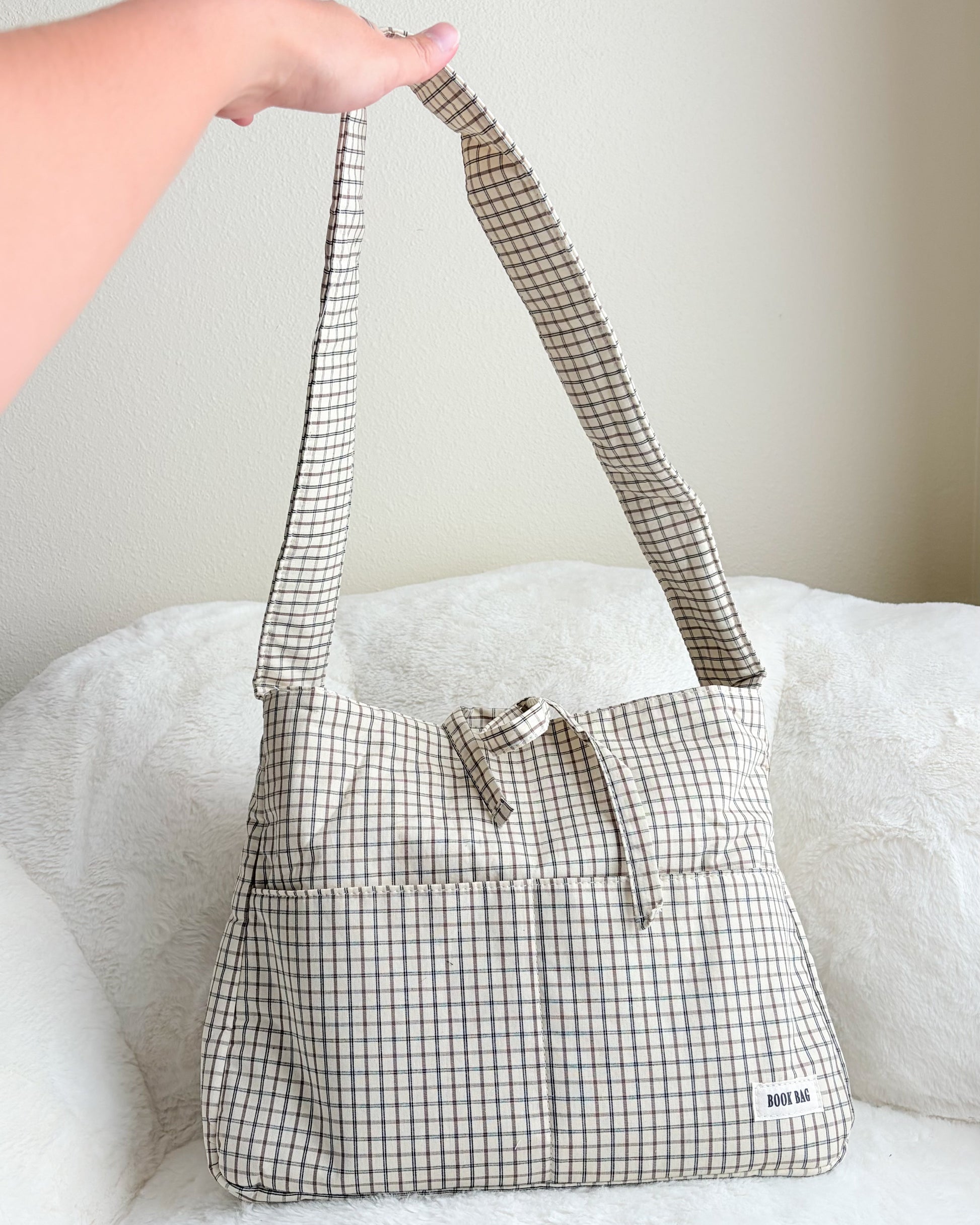 Plaid patterned handbag with a checkered strap held by a person on a white surface.