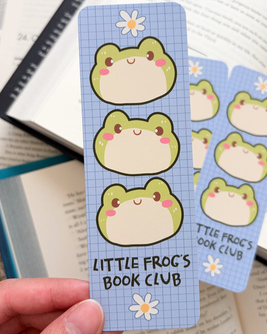 Cartoon frog bookmark with 'Little Frog's Book Club' text held by a hand over a book.