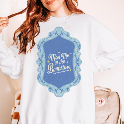 White sweatshirt with blue vintage frame graphic and 'Meet Me at the Bookstore' text.