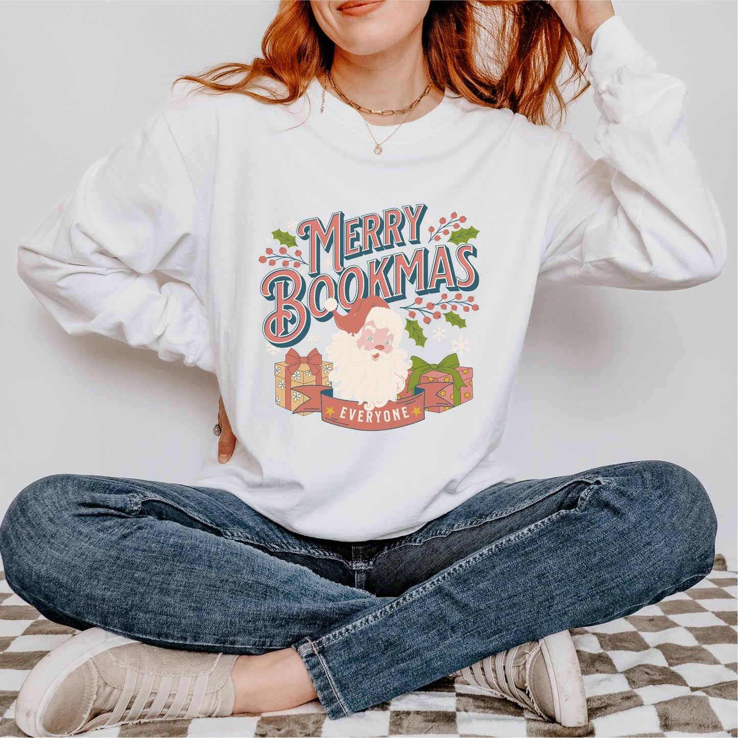 Woman wearing white Merry Bookmas sweatshirt with Santa, holly, and wrapped gifts graphic