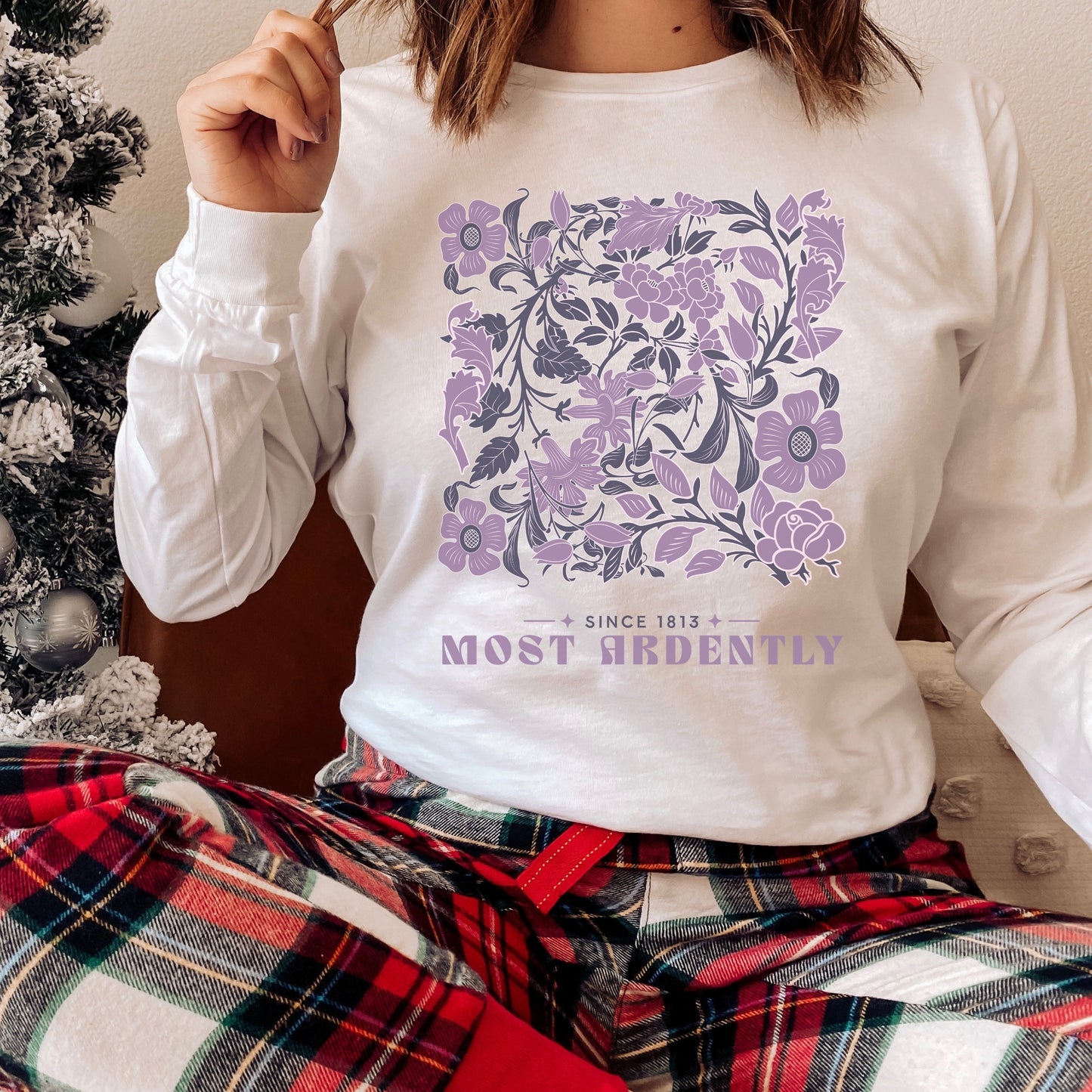 White long sleeve shirt with purple floral design and 'Most Ardently' text, worn casually indoors.