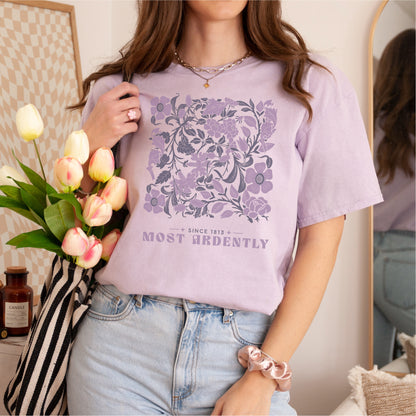 Woman wearing lavender 'Most Ardently' floral graphic tee, holding tulips in striped bag.
