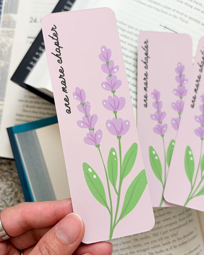 Pink floral bookmark with purple flowers and 'one more chapter' text held over open books