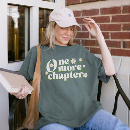 Woman in casual outfit holding book, wearing green 'One more chapter' book lover t-shirt with flowers