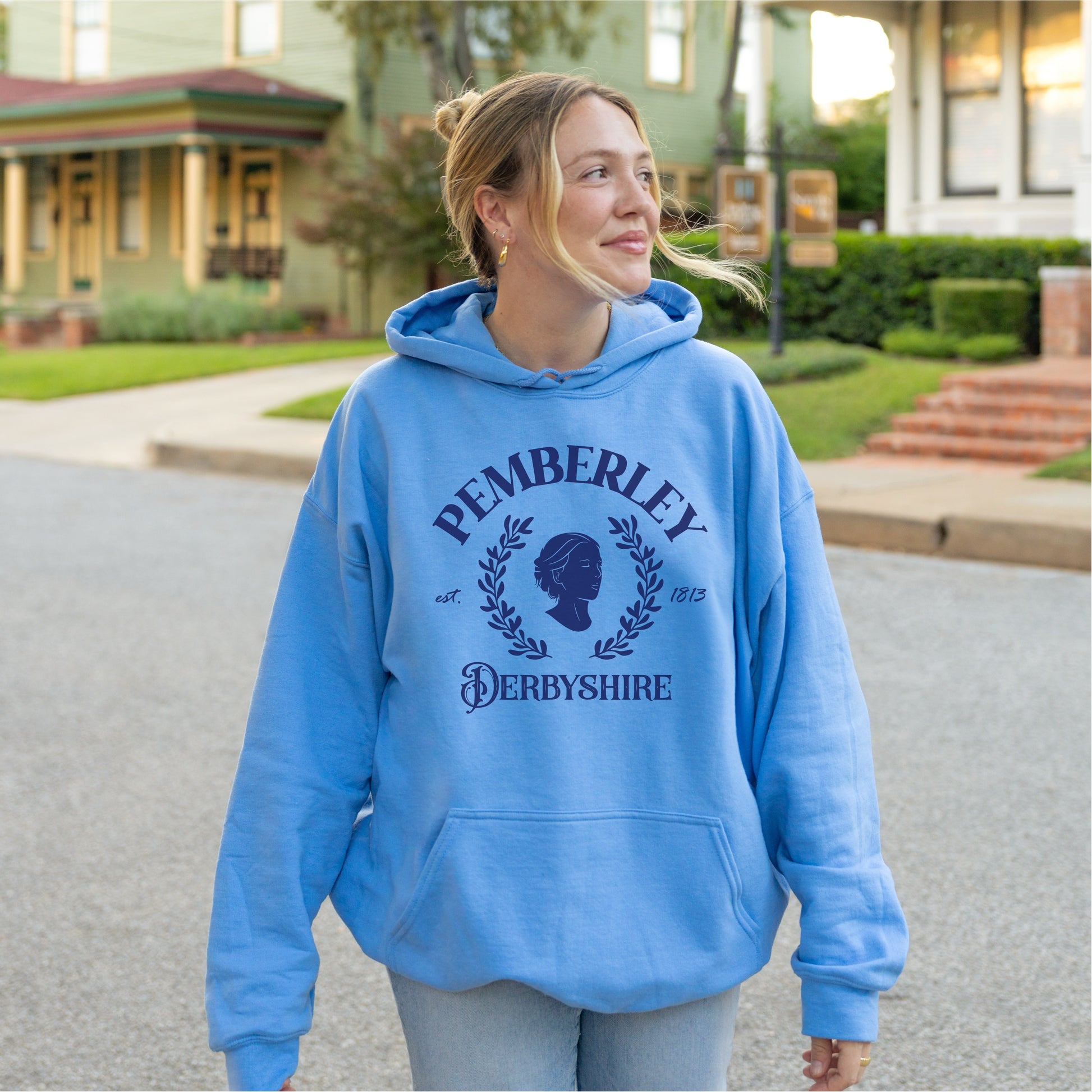 Woman in a blue Pemberley Derbyshire hoodie, standing outdoors on a residential street