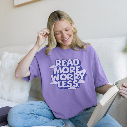 Woman reading on couch wearing lavender t-shirt with 'Read More Worry Less' slogan