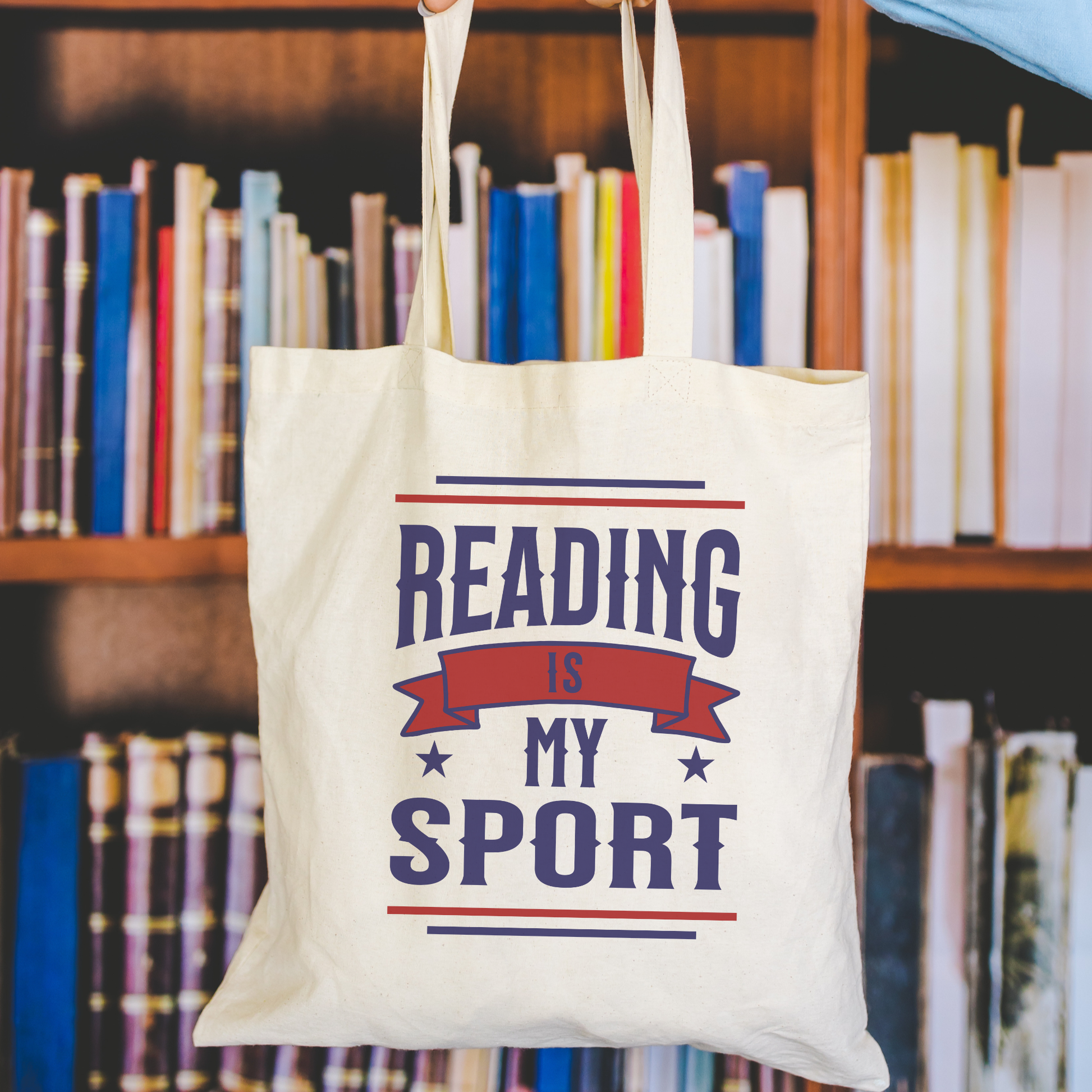 Organic cotton tote bag with 'Reading Is My Sport' text, held in front of bookshelves