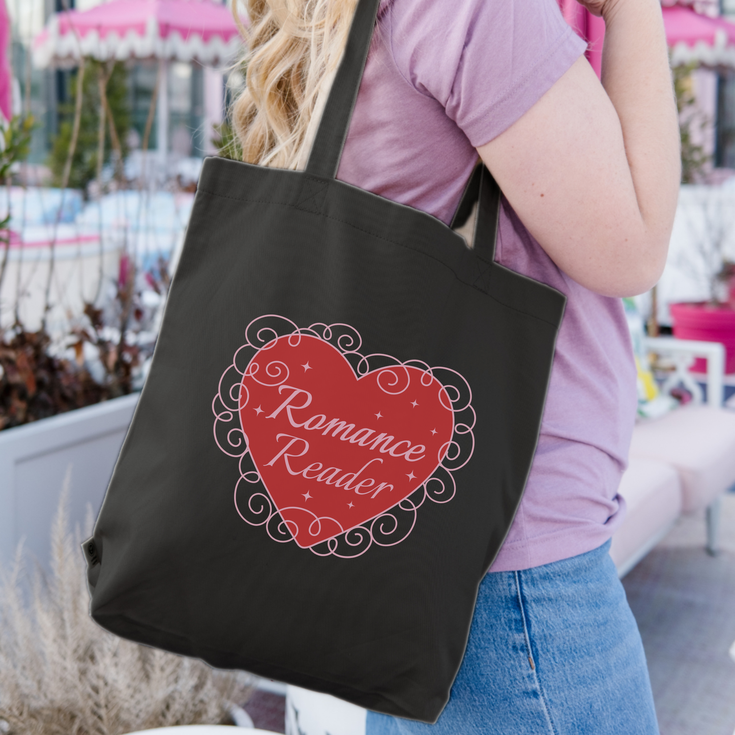 Black tote bag with 'Romance Reader' heart design, carried by woman outdoors