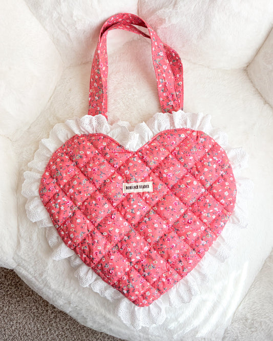 Pink heart-shaped bag with white ruffles on a white cushion