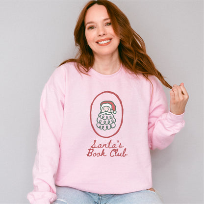 Woman wearing a pink Santa's Book Club sweatshirt with a Santa graphic and script text.