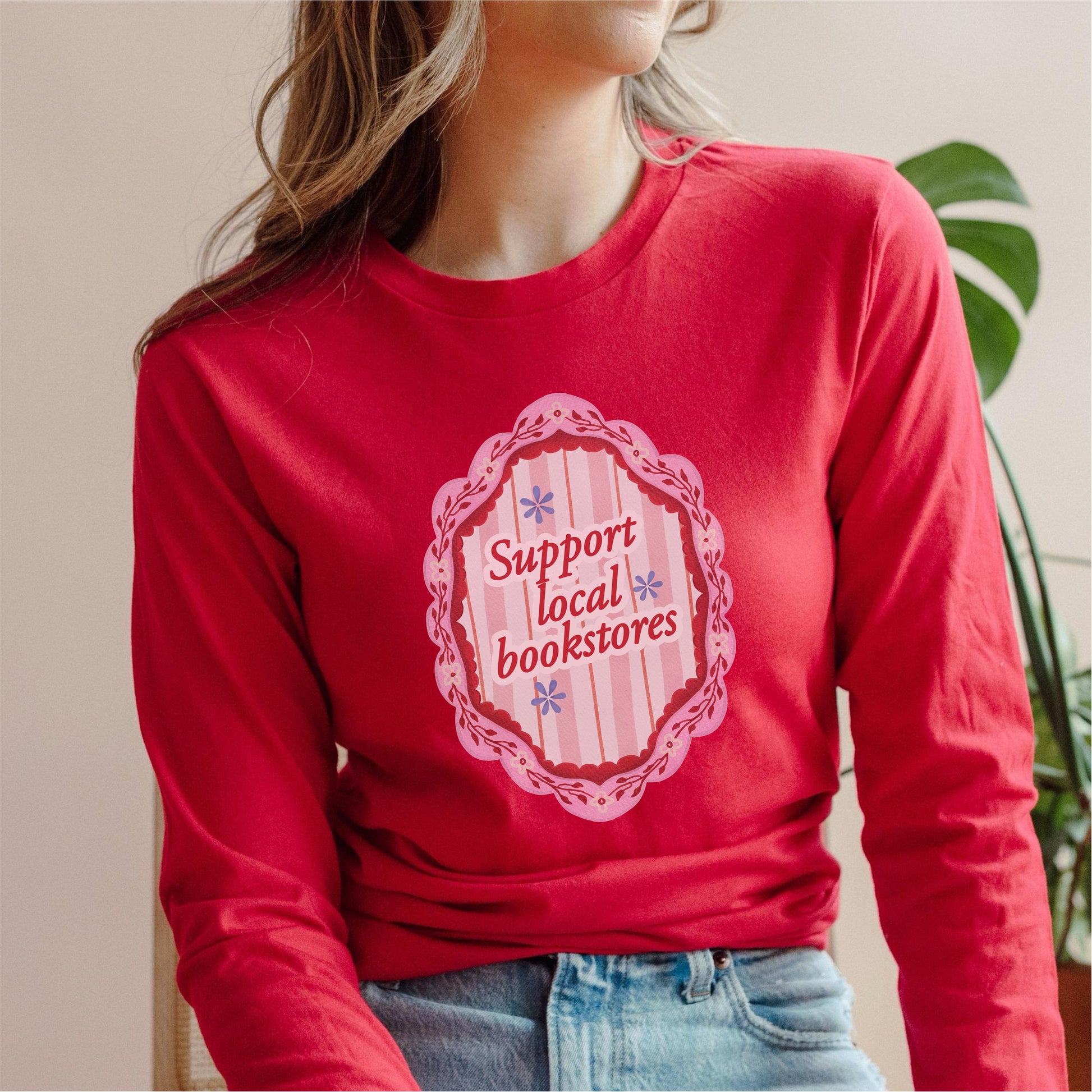 Red long sleeve shirt with 'Support local bookstores' pink graphic, worn by a woman