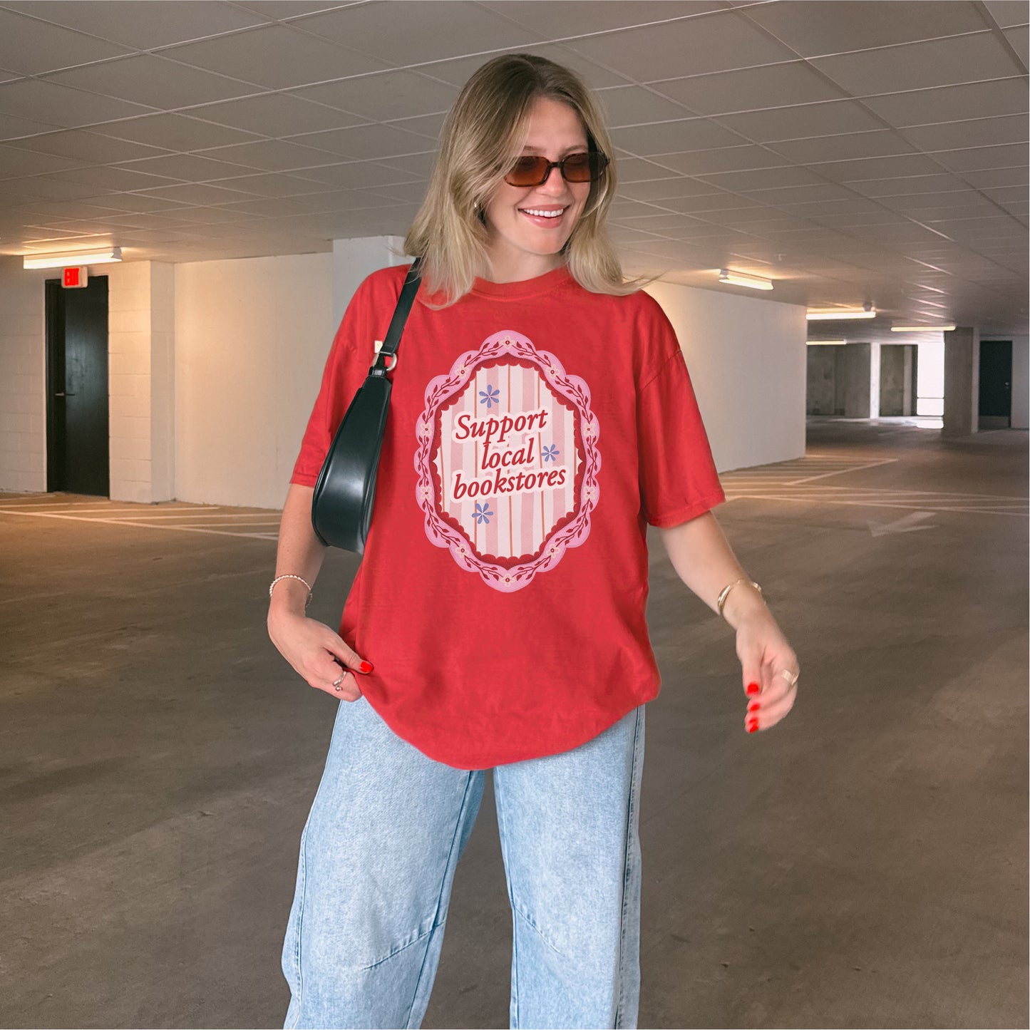 Woman wearing a red 'Support Local Bookstores' t-shirt and light blue jeans in parking garage