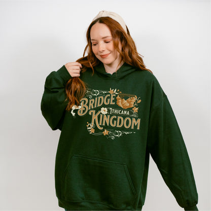Woman wearing dark green hoodie with 'Bridge Kingdom Thicana' book-themed graphic design