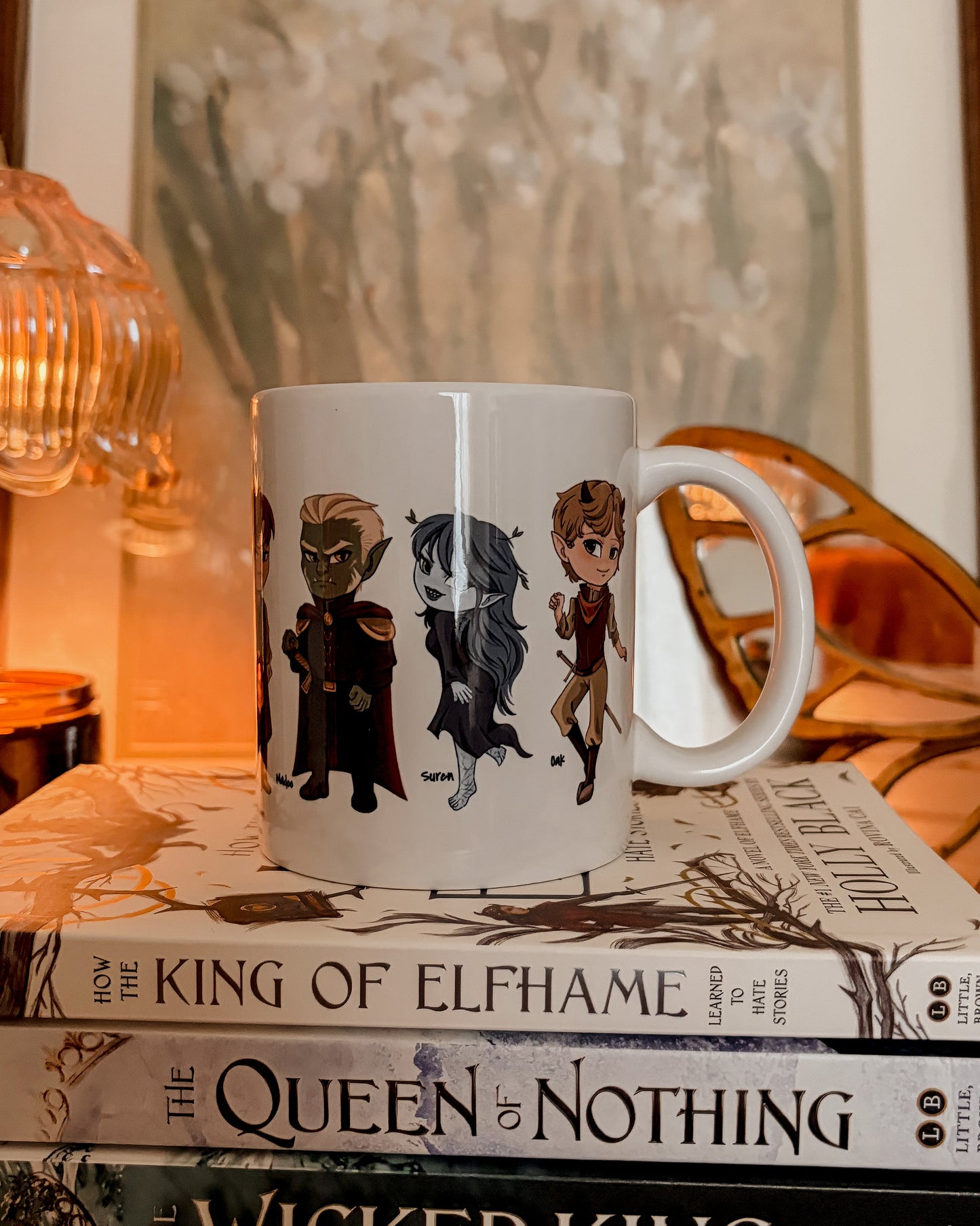 Mug with character designs on a stack of books titled 'The King of Elfhame' series.
