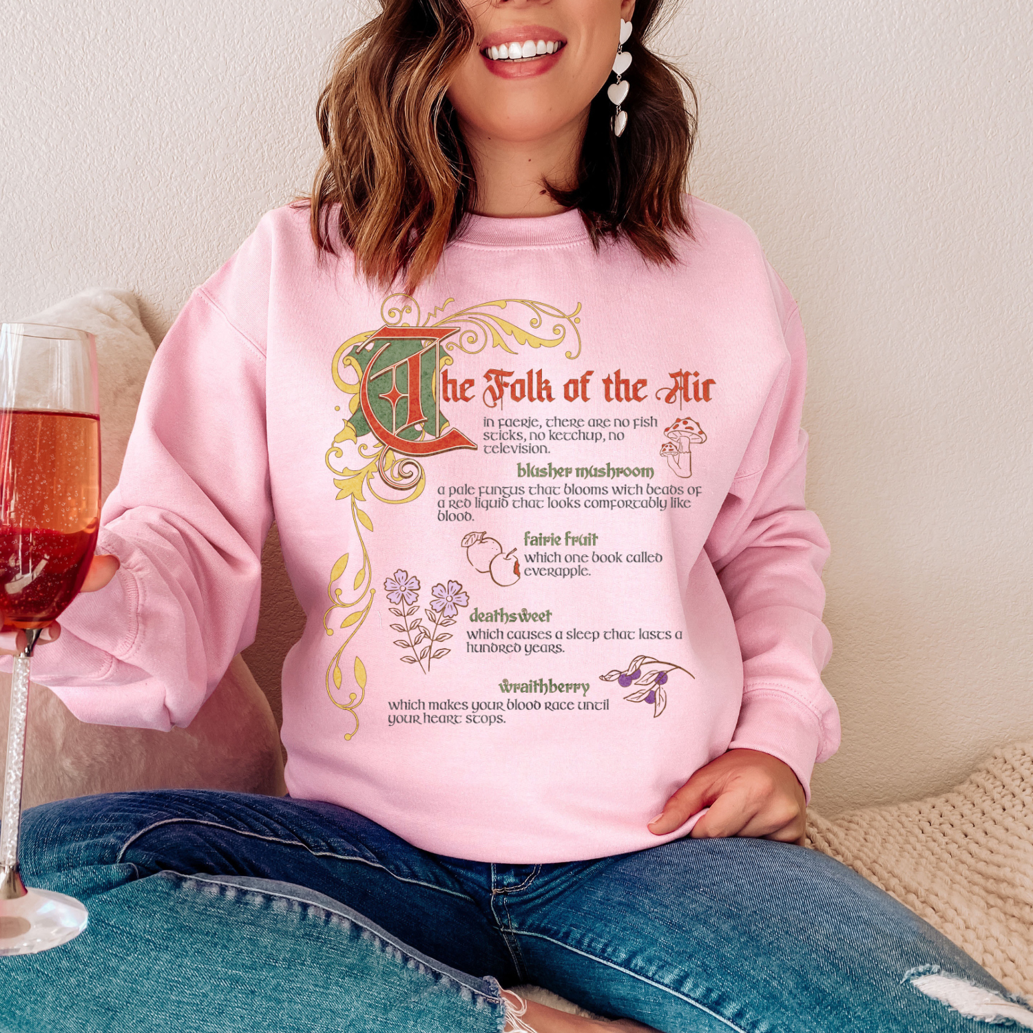 Woman wearing pink The Folk of the Air bookish sweatshirt with fantasy-themed design and text.