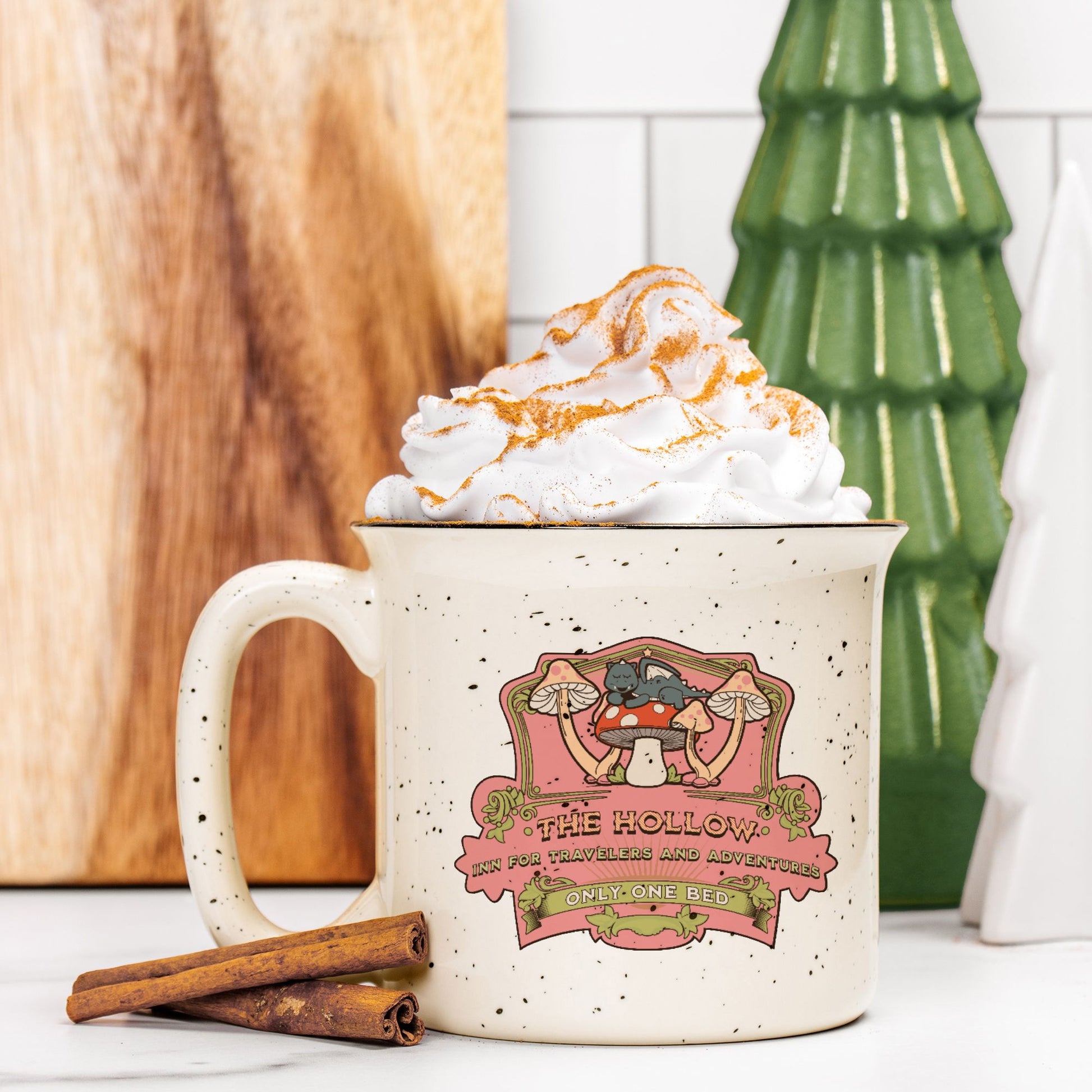 Speckled cream ceramic camp mug with whimsical mushroom illustration, topped with whipped cream.