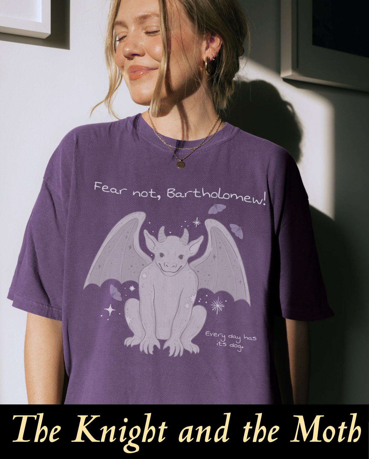 An officially licensed character merch t-shirt for Rachel Gillig's book The Knight and the Moth, showcasing the cute gargoyle Bartholomew printed in soft lavender on a deep purple comfort colors tee.