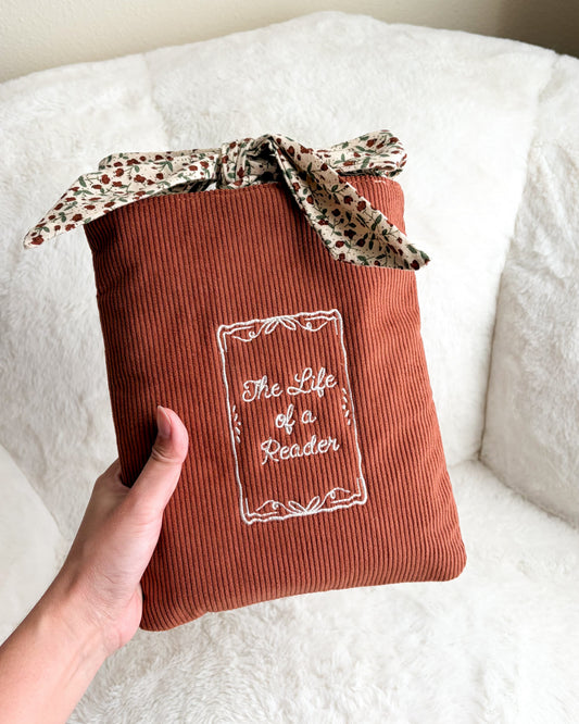 Brown book sleeve with 'The Life of a Reader' embroidery on a white surface