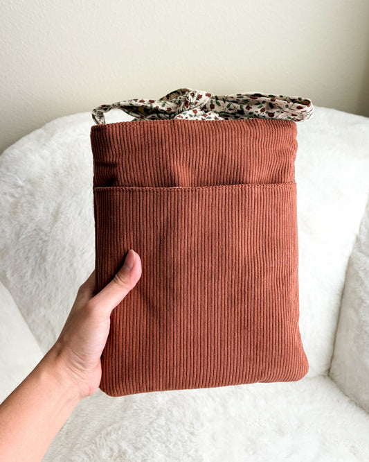 Brown corduroy pouch held by a hand on a white surface