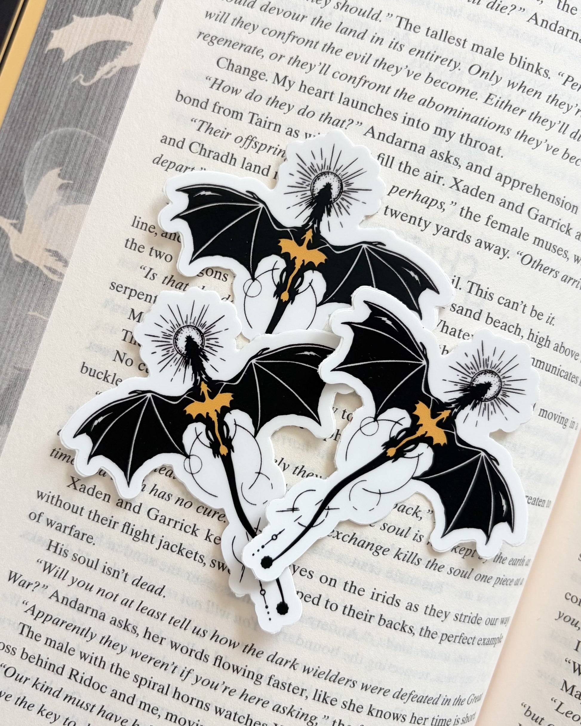 Black and gold dragon relic stickers on open book page, fantasy bookish merchandise