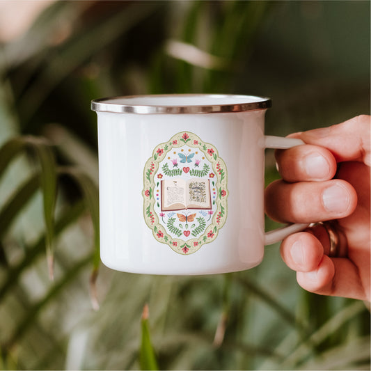 Hand holding white enamel mug with whimsical folklore book and floral design