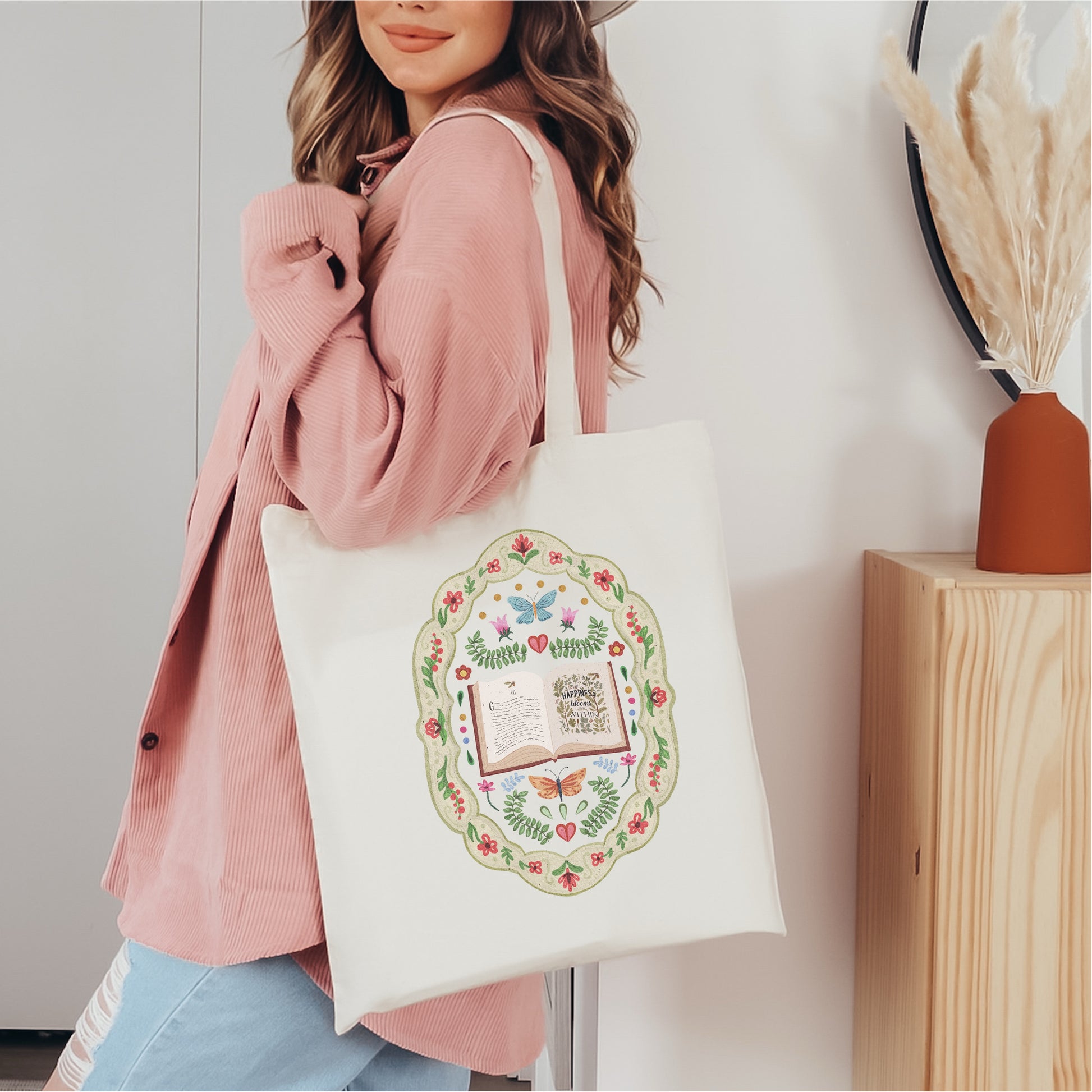 Woman carrying a white tote bag with whimsical book and floral folk art design