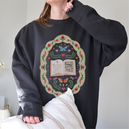 Woman wearing dark sweatshirt with open book and whimsical folklore floral design