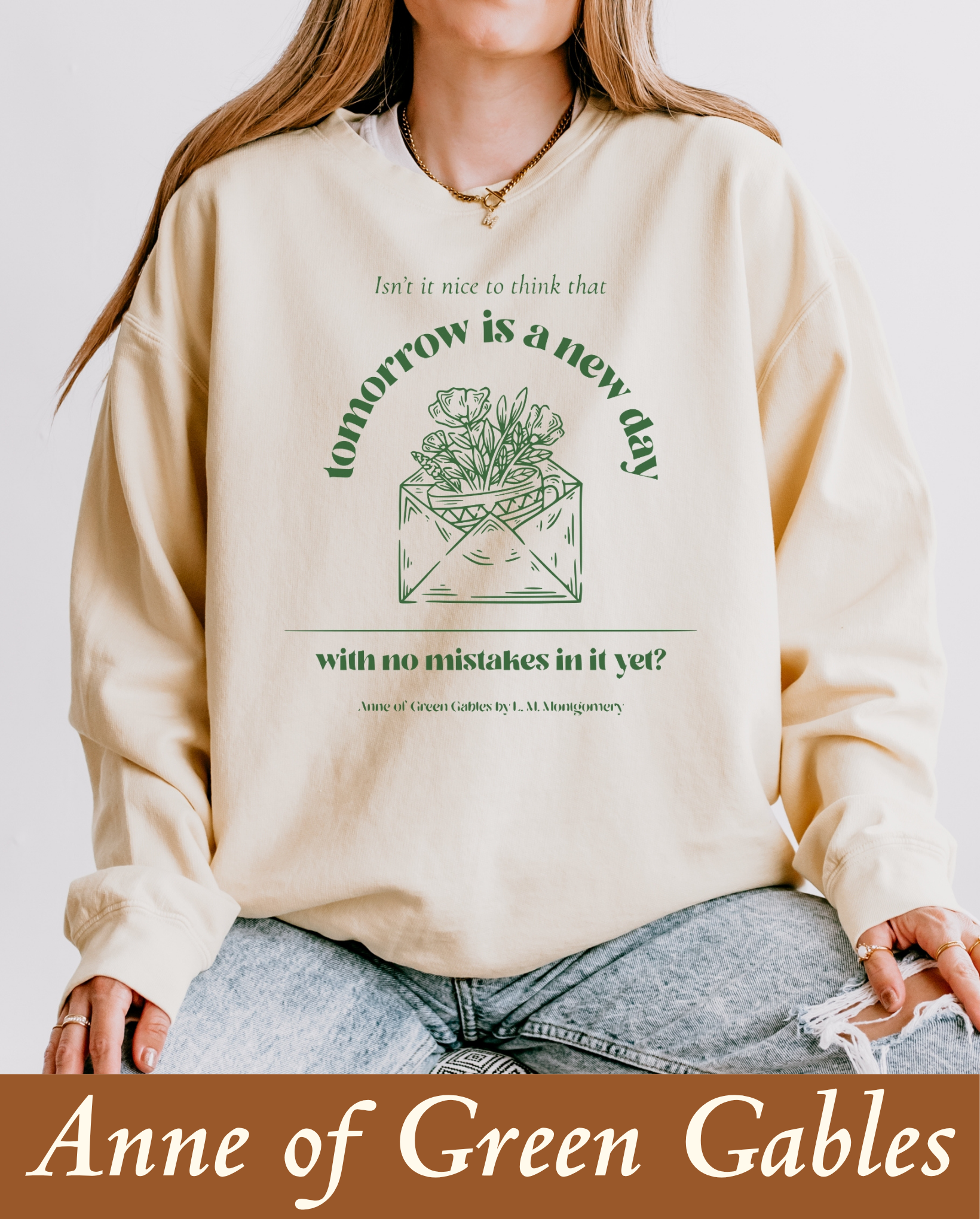 A model wearing a cozy cream crewneck sweatshirt featuring a sage green graphic design of an open envelope filled with blooming flowers. The text reads: 'Isn't it nice to think that tomorrow is a new day with no mistakes in it yet? - Anne of Green Gables by L. M. Montgomery.