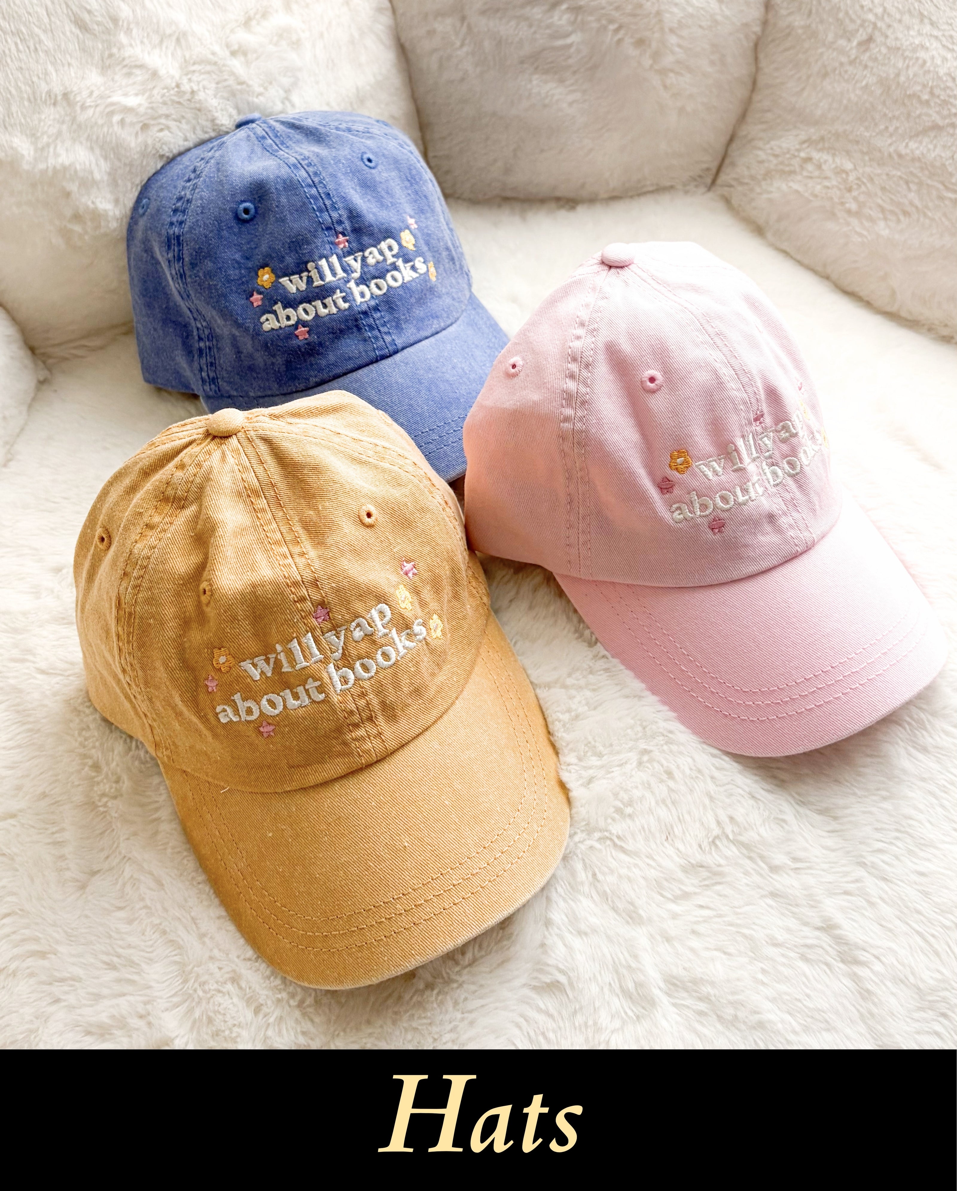 A collection of cozy, embroidered bookish baseball caps for readers, styled on a textured soft white backdrop for a casual, modern BookTok reading setting.