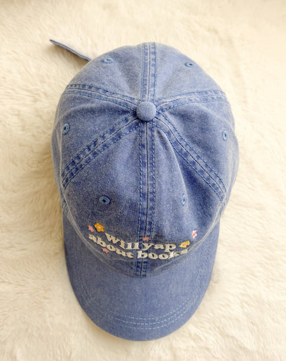 Blue denim cap with embroidered 'Will yap about books' text and small colorful flowers