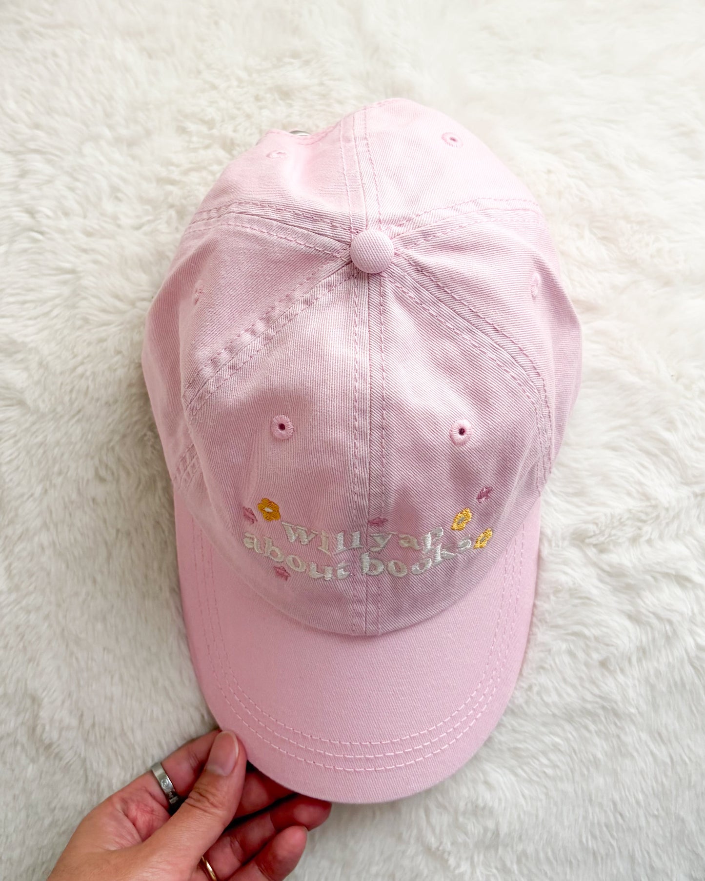 Light pink embroidered baseball cap with 'will yap about books' text and floral accents on white background