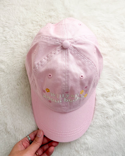 Light pink embroidered baseball cap with 'will yap about books' text and floral accents on white background