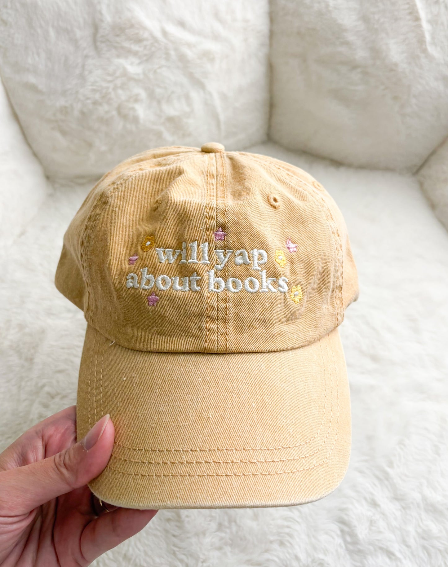 Beige embroidered baseball cap with 'will yap about books' text and pastel accents